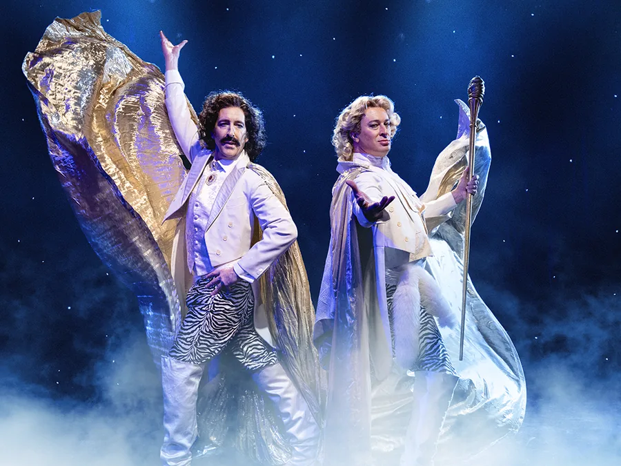 Two performers as Siegfried and Roy in white suits and gold capes, posing in stage smoke